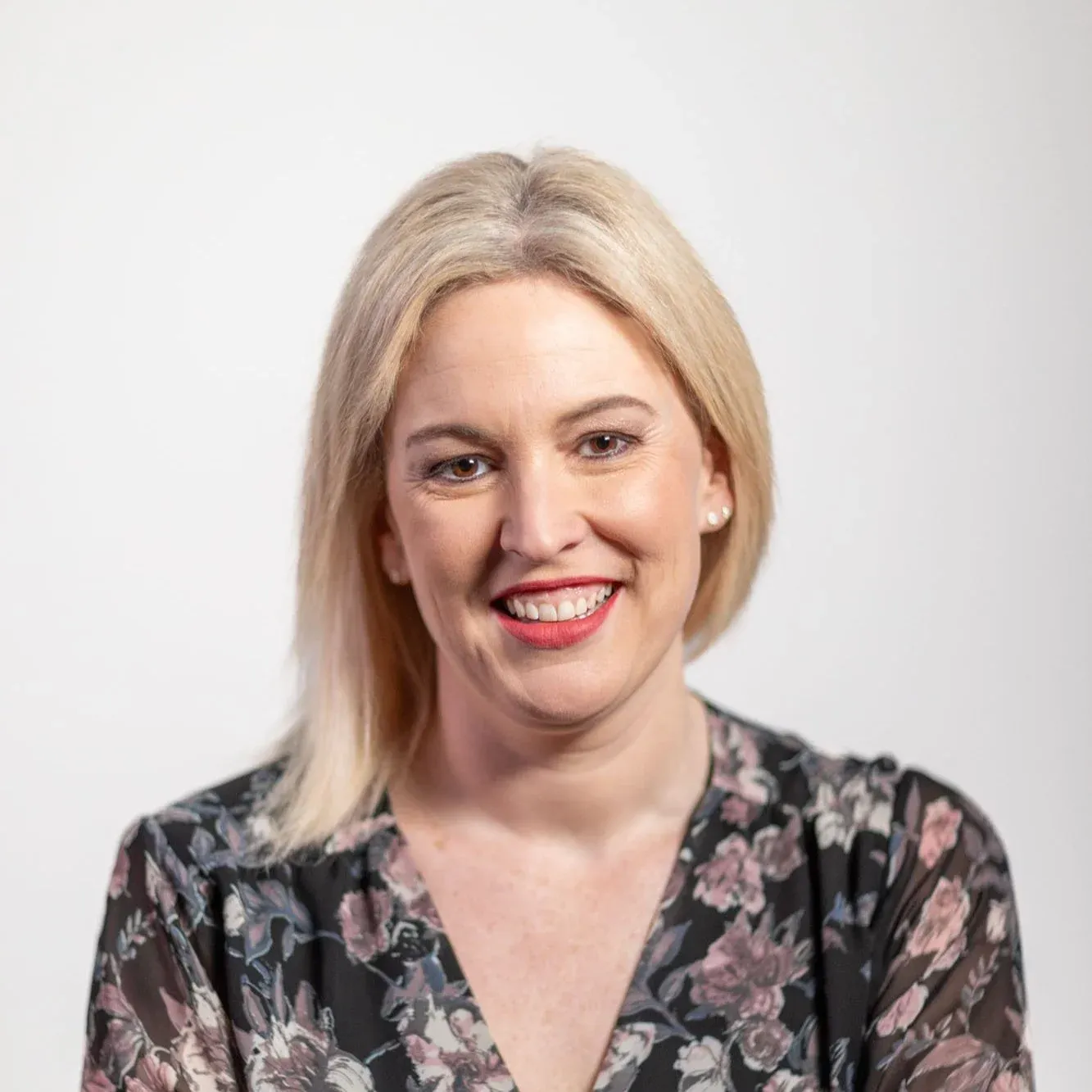 Portrait of a smiling woman with blonde hair and a floral blouse against a plain white background.