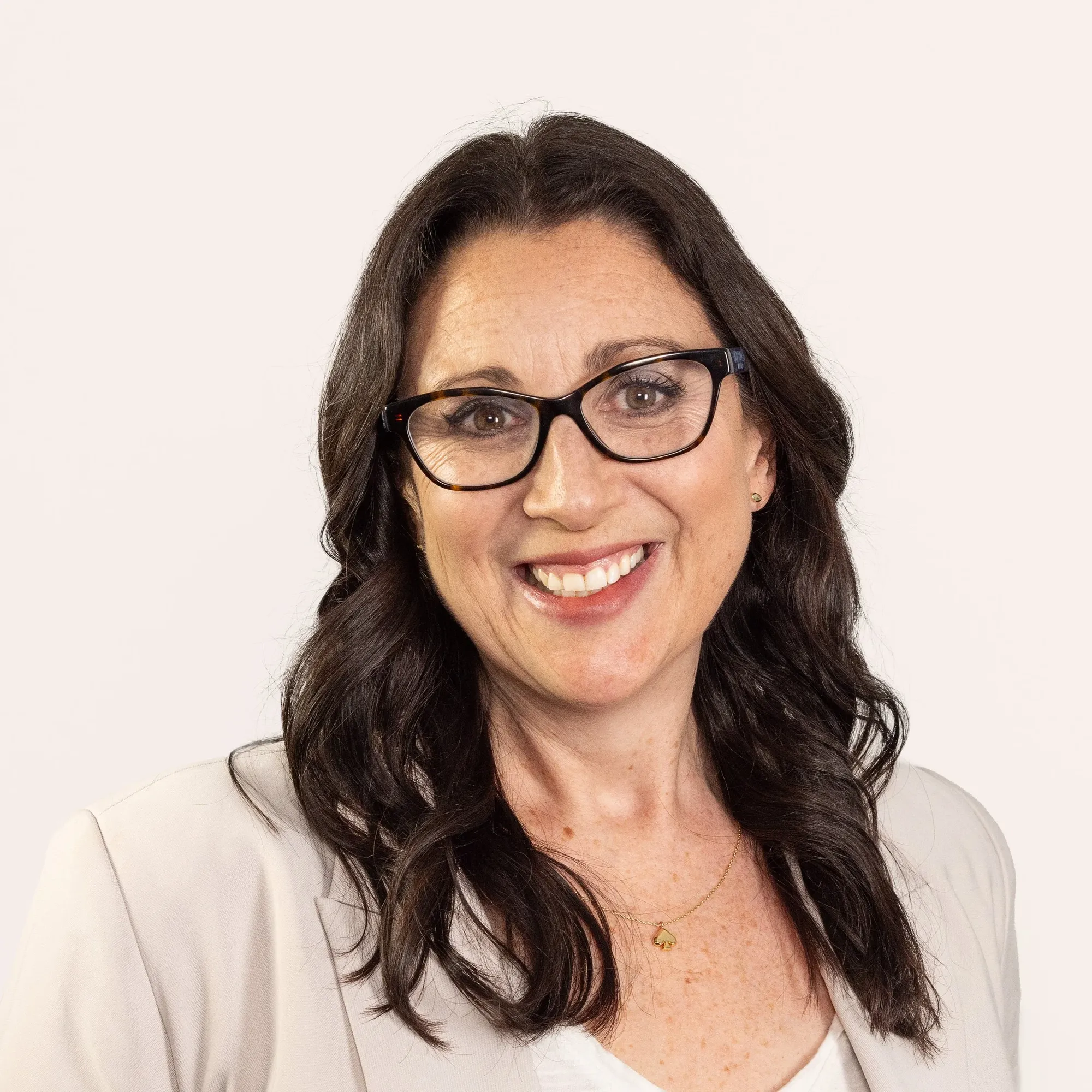 A woman with long dark hair, glasses, and a white blazer smiling against a plain white background.