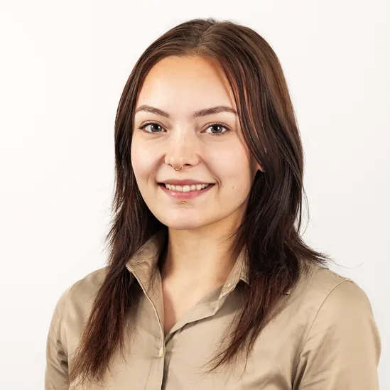 A young woman with brown hair smiling and wearing a beige button-up shirt against a white background.